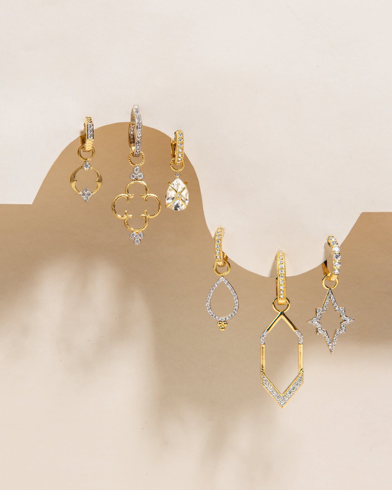 Different styles of gold earrings with diamonds, hanging off of a wave like display