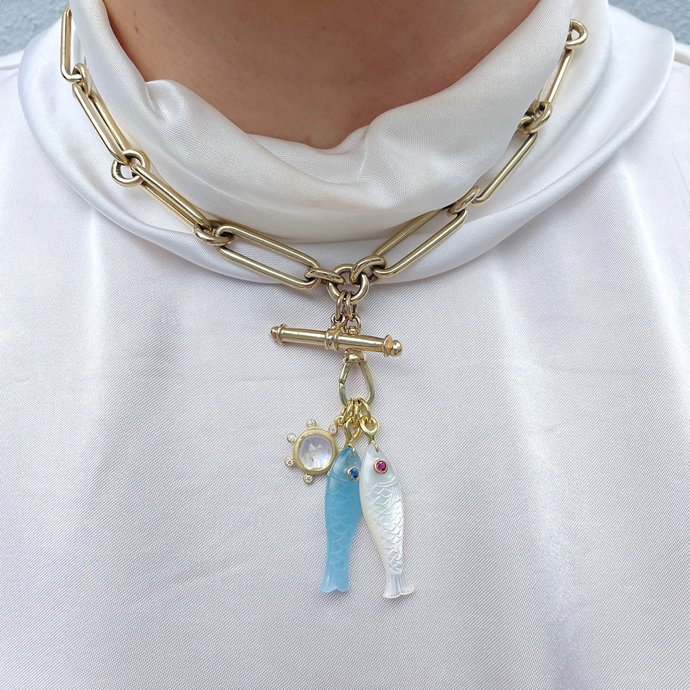 person wearing a white pendant next to a blue pendant on a thick gold chain